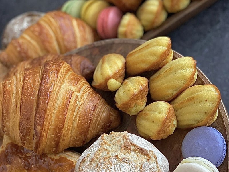Croissants, Madeleines und Macarons auf einem Holzbrett