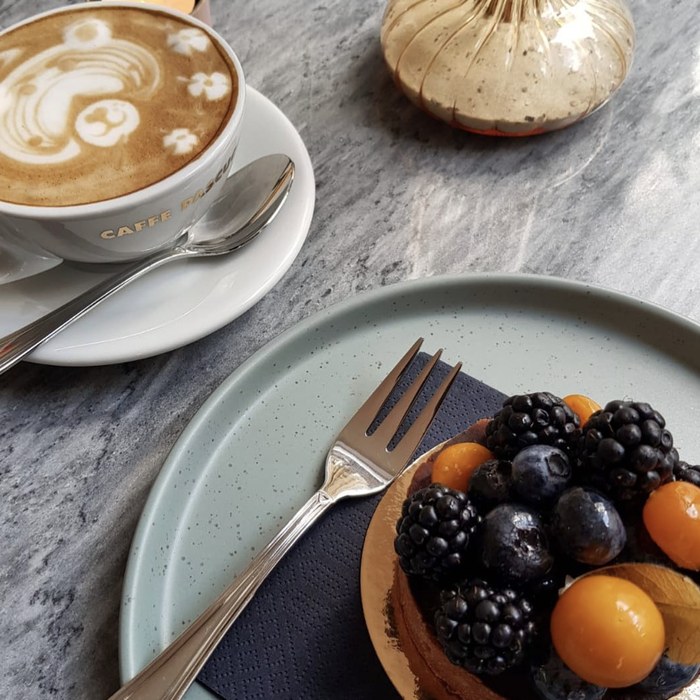 Kunstvolle Latte Art neben einer Beerentarte auf Marmor