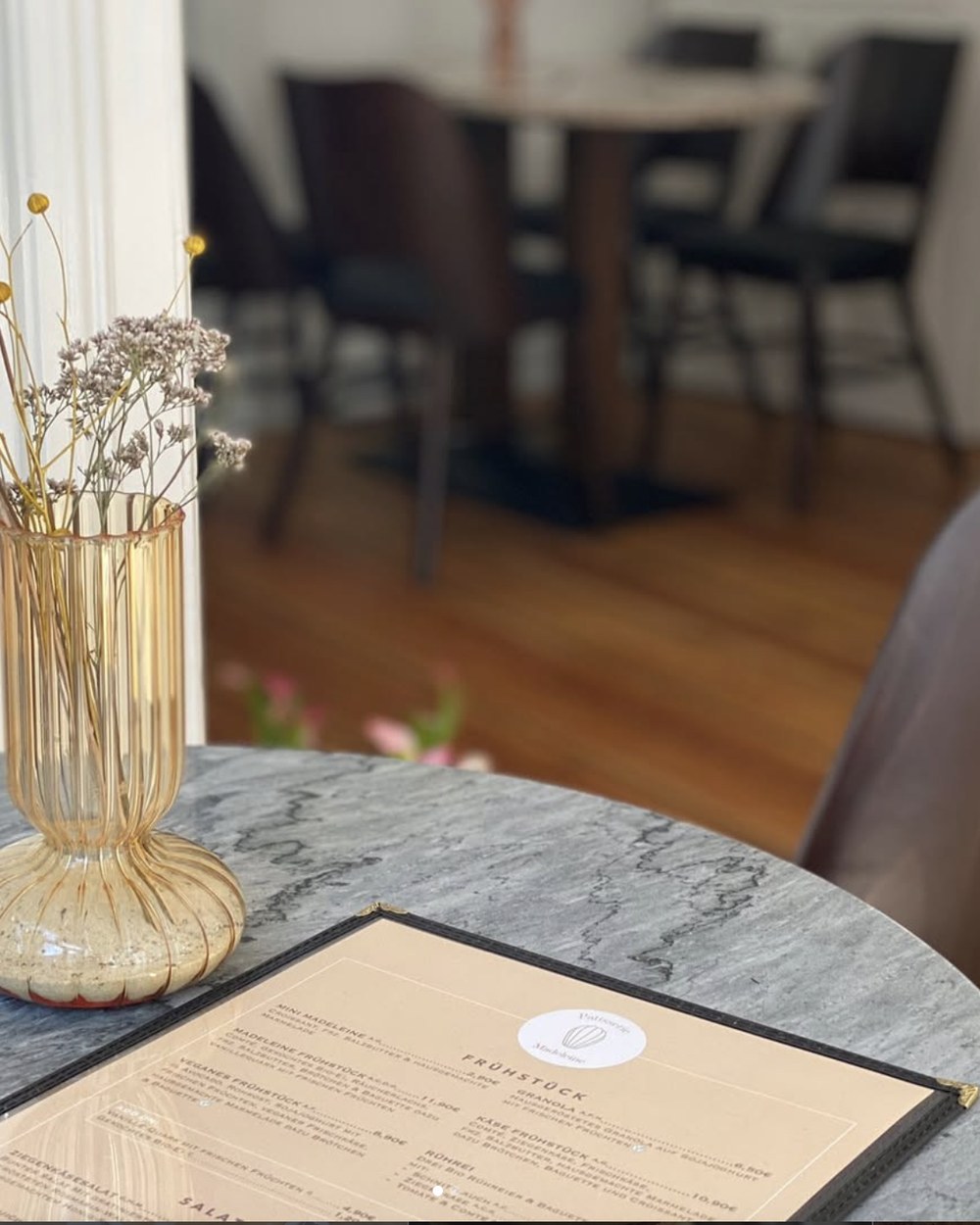 Marmortisch mit Speisekarte und Trockenblumen, im Hintergrund der Gastraum